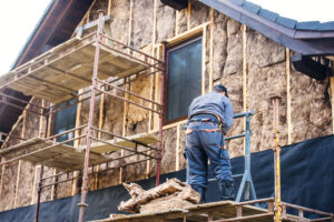 Construction worker standing on scaffold thermally insulating house facade with glass wool.
