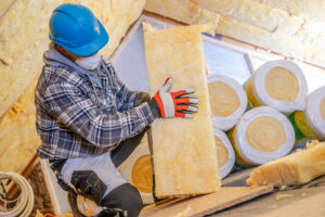 A construction worker is carefully installing insulation materials in a residential attic, wearing safety gear and ensuring proper fit for energy efficiency.